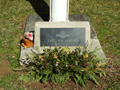 Concrete base of flagpole with marble plaque with text Lest We Forget next to floral wreath