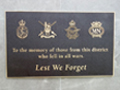 Bronze plaque with emblems of New Zealand military branches in gold under picture of a laurel wreath and heading Lest We Forget