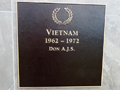 Square bronze plaque with a name in gold under picture of a laurel wreath and heading Vietnam 1962-1972