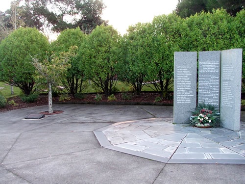 Marble memorial with text inscriptions on concrete tiles surrounded by trees.