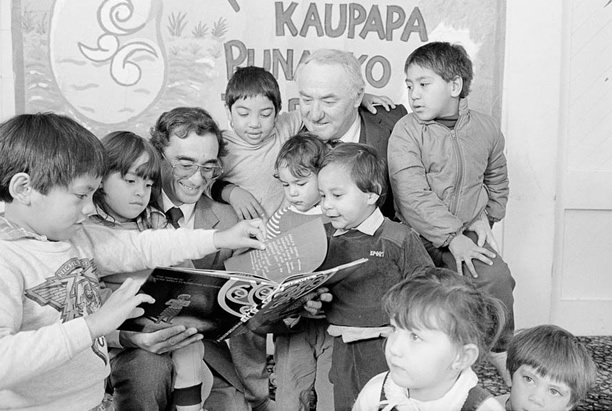 Children gathered around with two men and a book at a Kohanga Reo