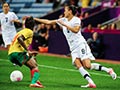 A woman in a New Zealand football uniform and a player in a Cameroon uniform compete for a ball.
