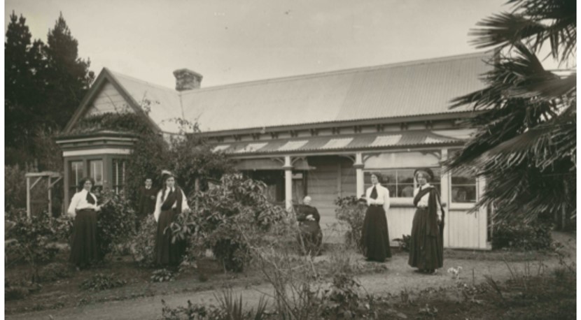 Photograph of house and garden with six people standing in the foreground