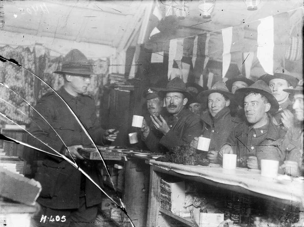 Men in uniforms sitting at bar eating cake and drinking from mugs.
