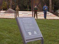 Plaque with text fixed into grass in front of handle shaped bronze memorial.