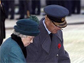 A woman and a man in blue military uniform about to place a foral wreath on the ground