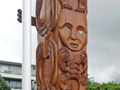 View of carved powhenua memorial to D Company 28th Māori Battalion with wreaths laid against the bottom of the pouwhenua.