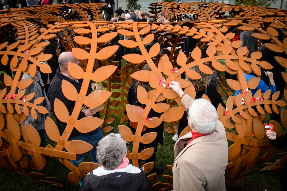 People placing red poppies on steel sculpture
