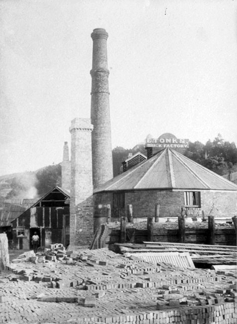 Piles of bricks in front of buildings with three tall chimneys