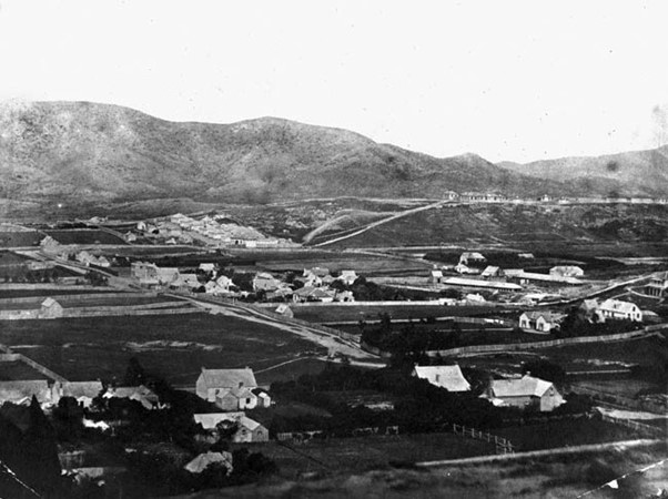 View of houses, fields and dirt roads with bare hills in the background