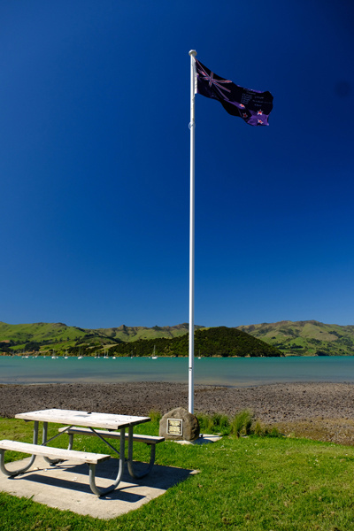 Flagpole next to picnic table with sea and boats in the background.