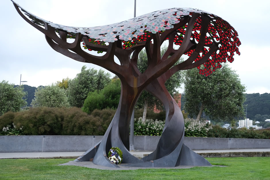 Stylised metal sculpture of two trees. A floral wreath sits in the roots.