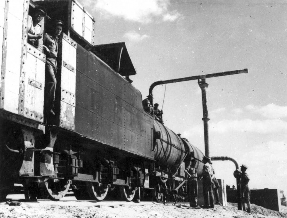 Men in uniform standing on and beside train engine and carriages.