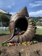 Bronze memorial in the shape of a conch shell covered in flowers