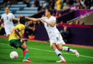 A woman in a New Zealand football uniform and player in a Cameroon uniform vie for the ball during a game.  