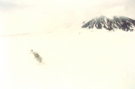 Dark smudge against a white snow with mountain in the background.