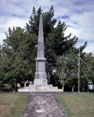 Stone obelisk set on lawn against stand of trees
