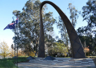 Handle-shaped bronze memorial set into concrete behind two flags and flagpoles.