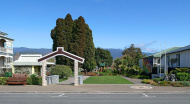 Grass park with Māori waharoa (gateway) in the foreground and mountains in the background
