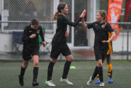 Three girls dressed in black football uniforms, playing football in the rain, high-five each other.