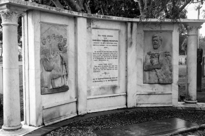 Marble stone memorial consisting of a central panel of text flanked by reliefs of human figures.