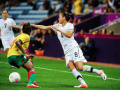 A woman in a New Zealand football uniform and player in a Cameroon uniform vie for the ball during a game.  