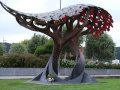 Stylised metal sculpture of two trees. A floral wreath sits in the roots.