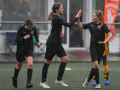 Three girls dressed in black football uniforms, playing football in the rain, high-five each other.