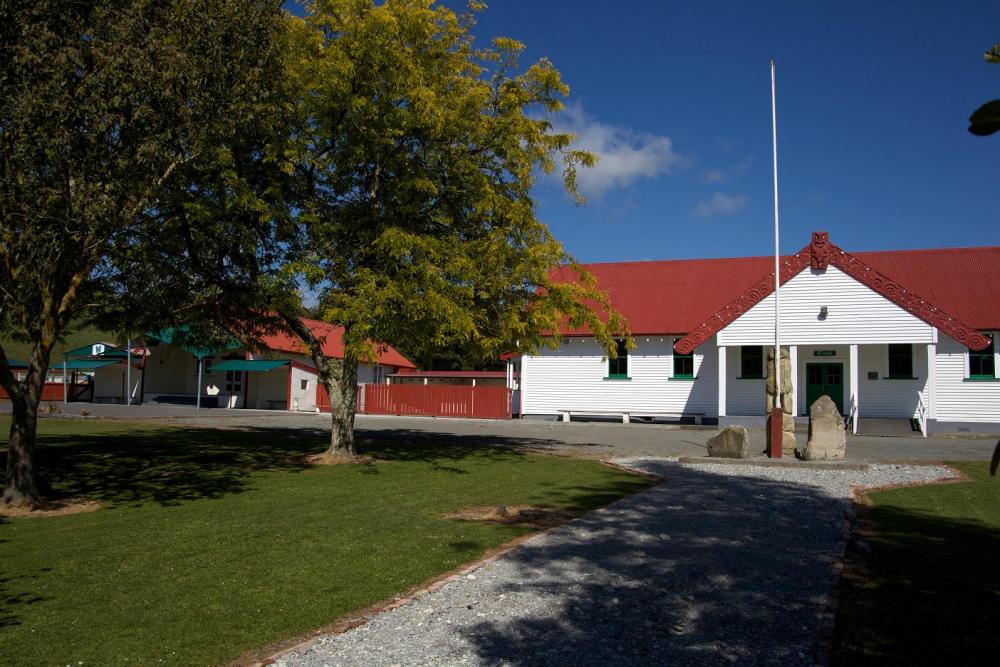 White building with red roof with grass, trees and a flagpole in the foreground