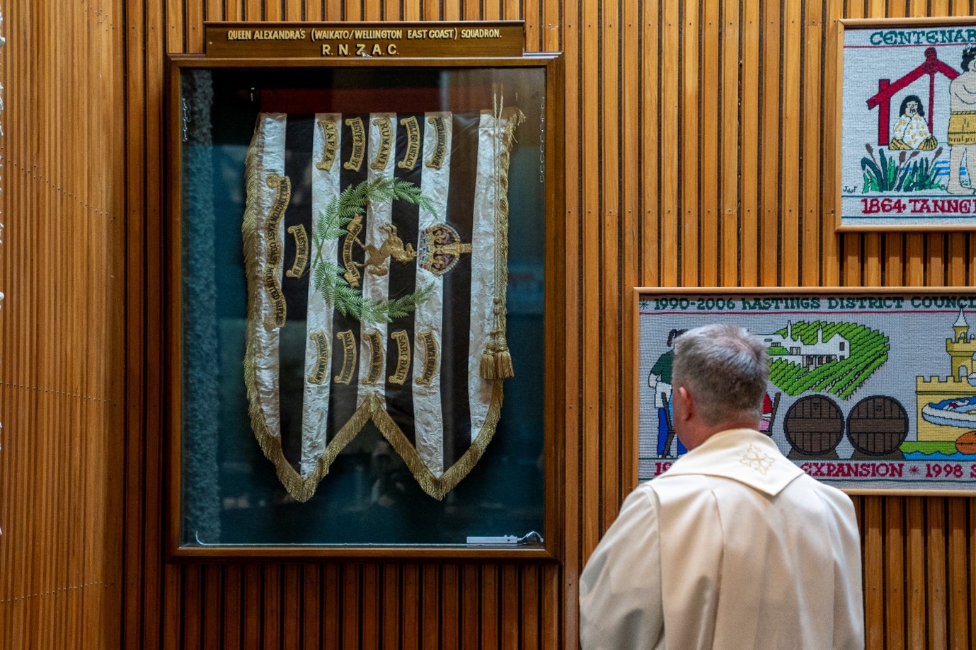 Person in religious robes looking at flag encased in glass fixed to wood-paneled wall. 