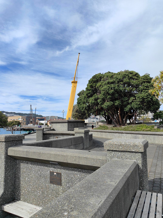 Yellow ships mast surrounded by concrete walls and large pohutukawa tree