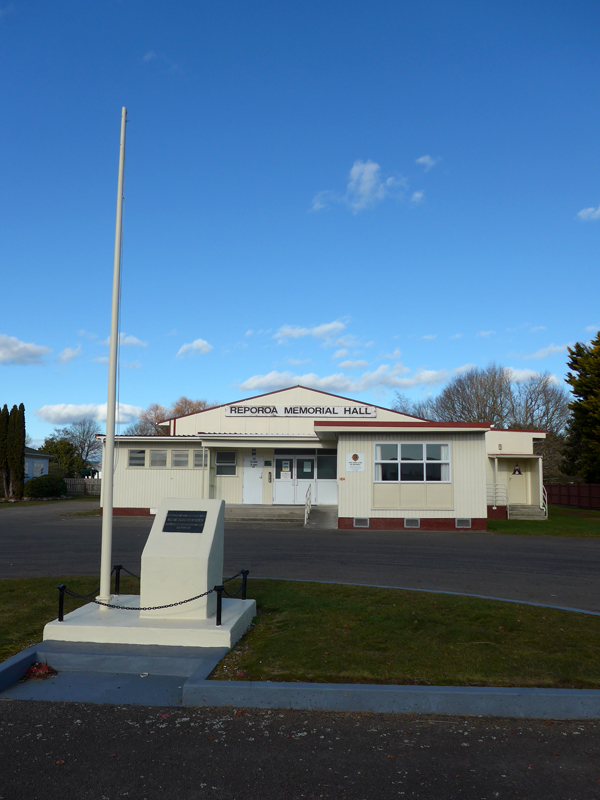 Flagpole and stone plinth in front of red and white building.
