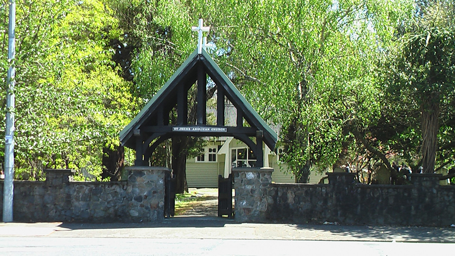 Large wooden lychgate and stone wall with leafy trees behind