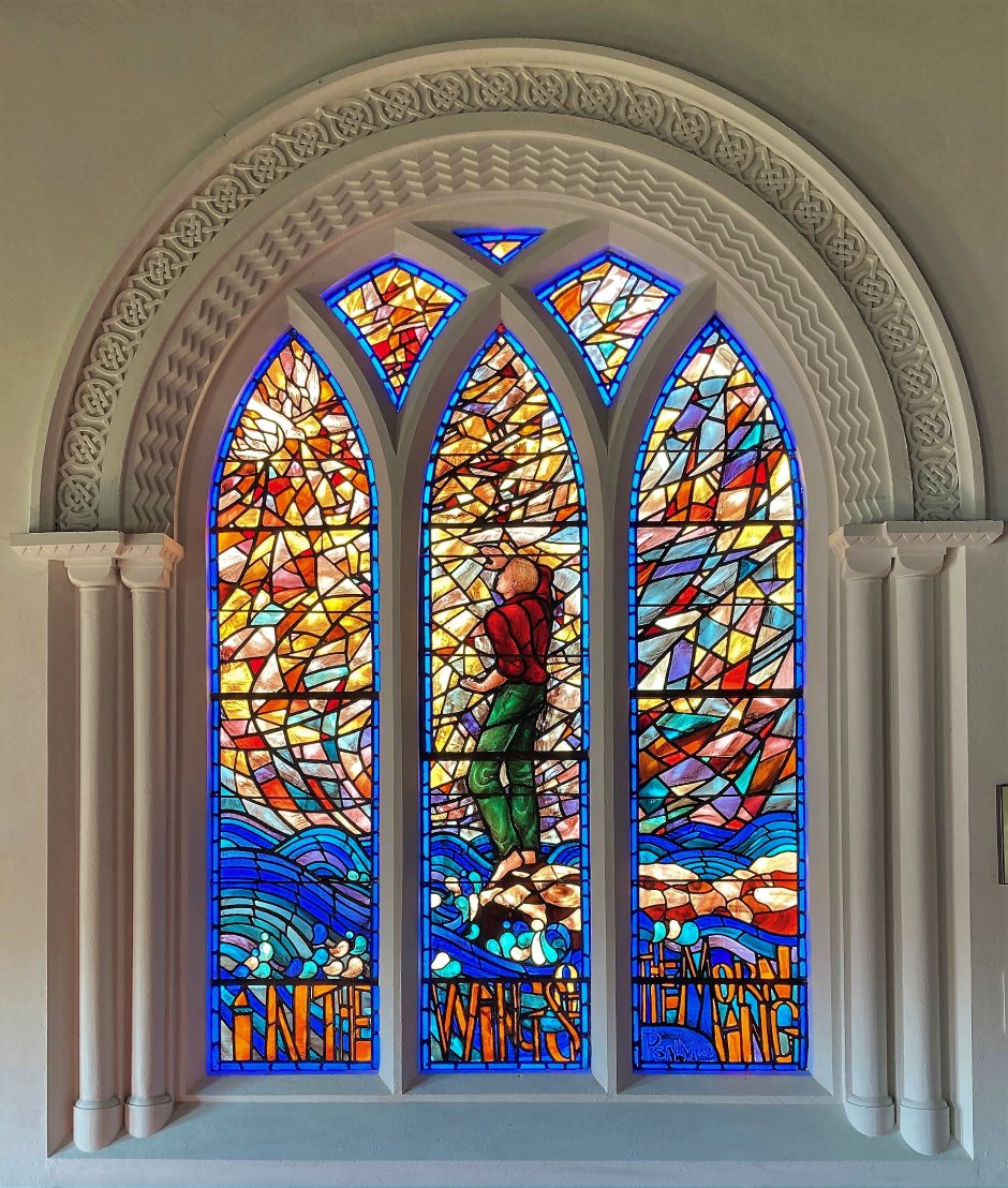 Stained-glass window with figure point to sky and words 'In the wings of the morning' along the bottom