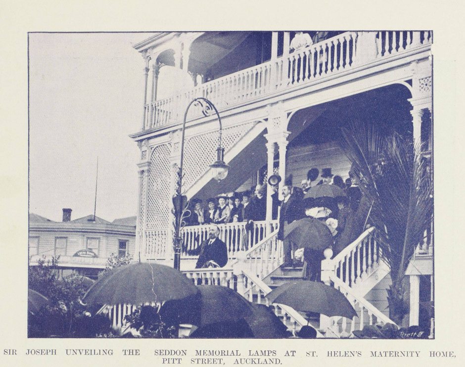 Historic image with crowd gathered on deck and grounds of two-storey wooden building with a lamp in front. One person is speaking to the crowdd