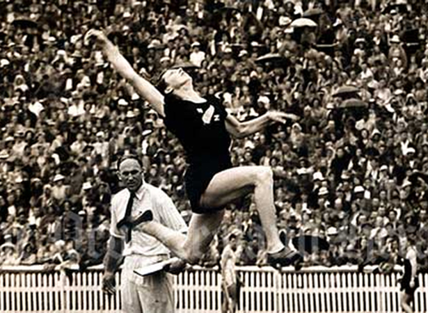 Woman in black sports uniform jumping through the air with huge crowd watching in the backgound 