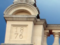 Top of facade of stone building with dates 1876 and 2006 engraved on each side