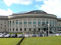 Exterior of large semi-circular stone building with carpark and lawn in front