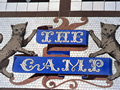Coat of arms in mosaic tiles featuring two cats either side of 'The Camp' written in white on blue