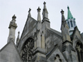 Spires and chimneys protruding from roof of stone church building