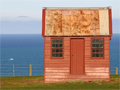 Single red wooden building in paddock with ocean in background
