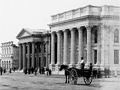 Historical image showing street with a Pennyfarthing bicyle and horse and carts with two Greek-style bank buldings on right