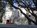Road frontage with white picket fence and wooden church behind two large trees