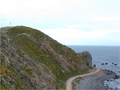 Lighthouse poking up behind hill near coastal track