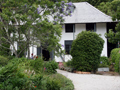 Two-storey house with white plaster walls and slightly curved tiled roof behind garden