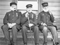Three old men in uniform smoking pipes while seated on deck.