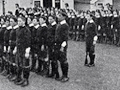 Cadets standing in straight rows in on lawn in front of buildings