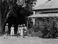 Historic image showing corner of wooded house with five people gathered on the lawn in front