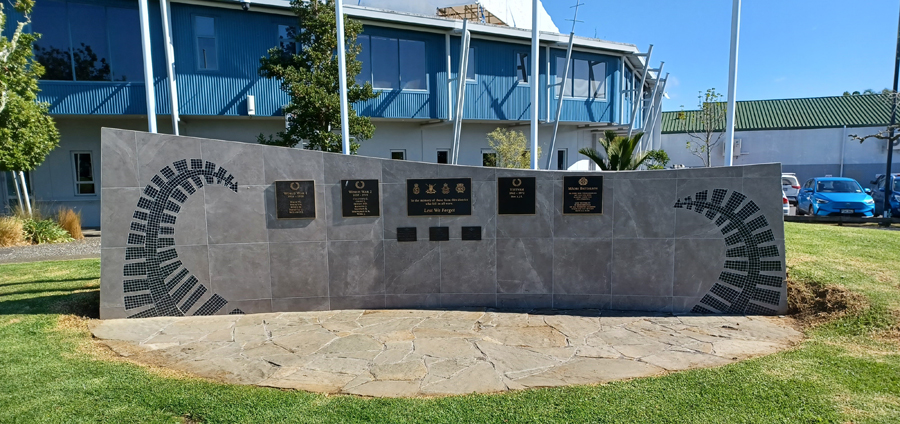 Concrete wall with bronze plaques attached and curve mosaic pattern at either end