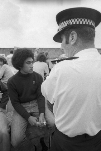 Seated young man looking up at policeman standing with arms folded